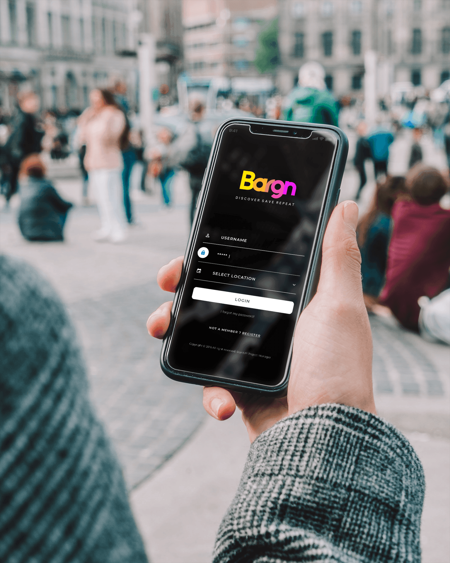 Person holding a smartphone displaying the login screen of the Bargn app with a blurred urban background.