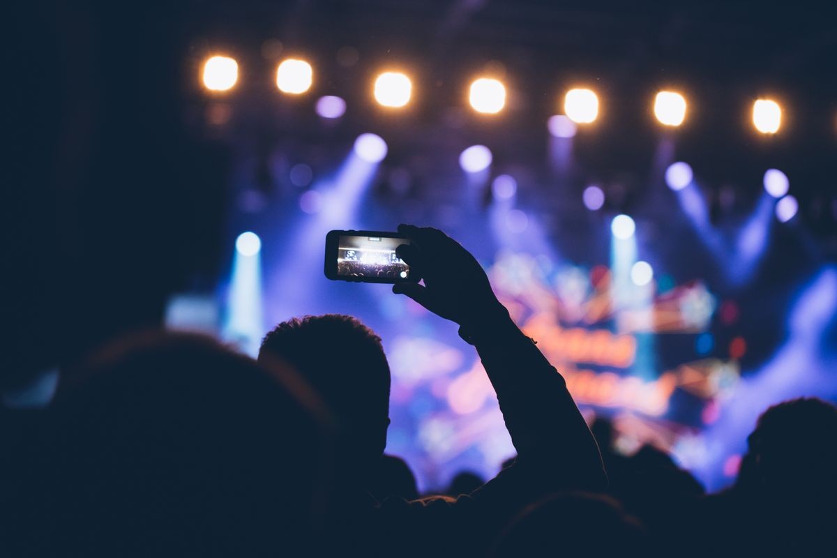 Stage lights and crowd of audience with hands raised at a music festival.