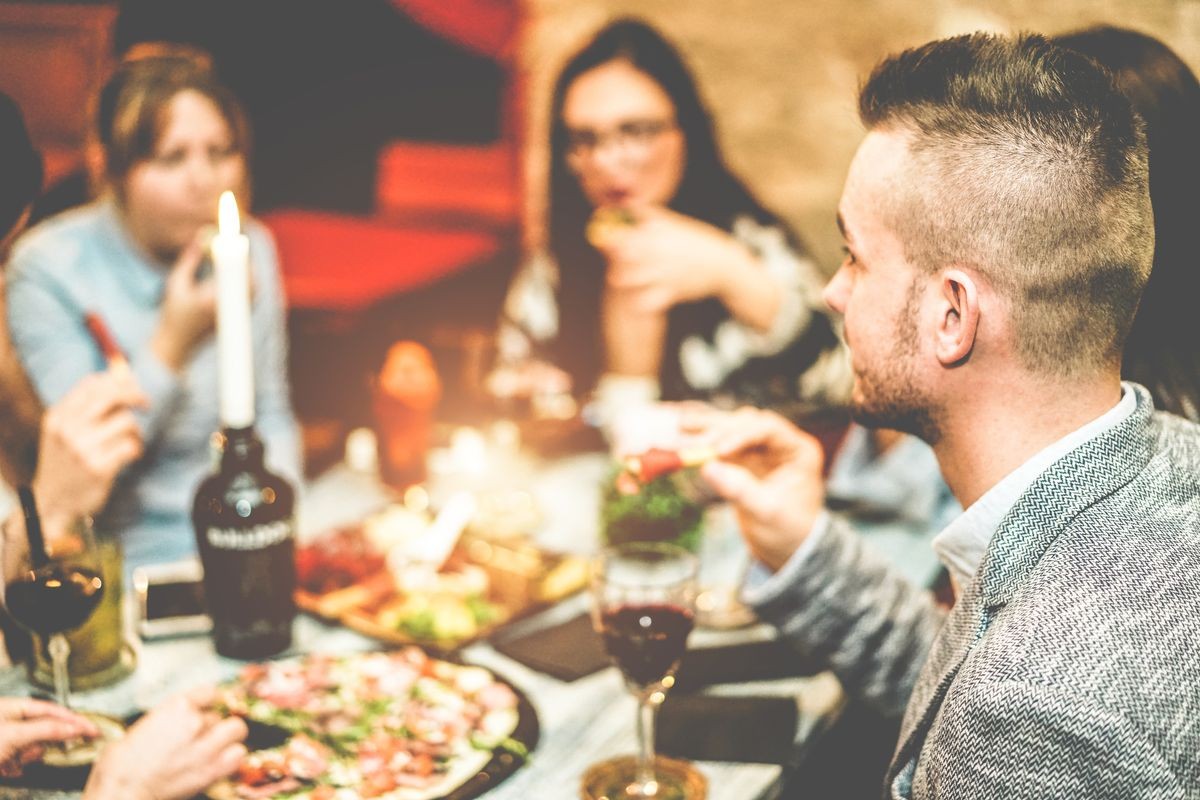 Group of friends drinking appetizer in vintage american bar - Young people eating finger food and drinking tropical fruits cocktails - Nightlife, party and dinner concept - Focus on right man ear