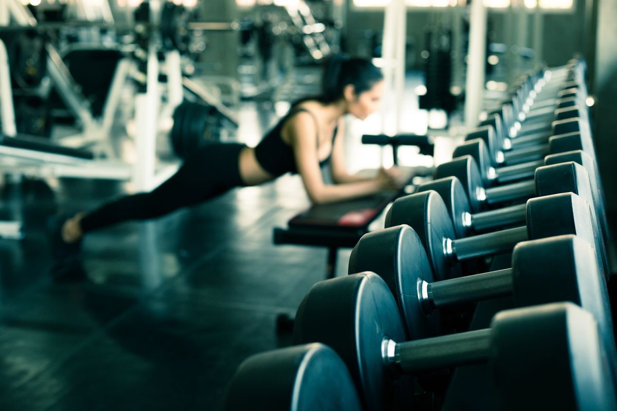 gym interior with equipment,Rows of dumbbells in the gym.Dumbbells in gym with Blurred background Young beautiful woman doing exercises , Weight Training Equipment concept.